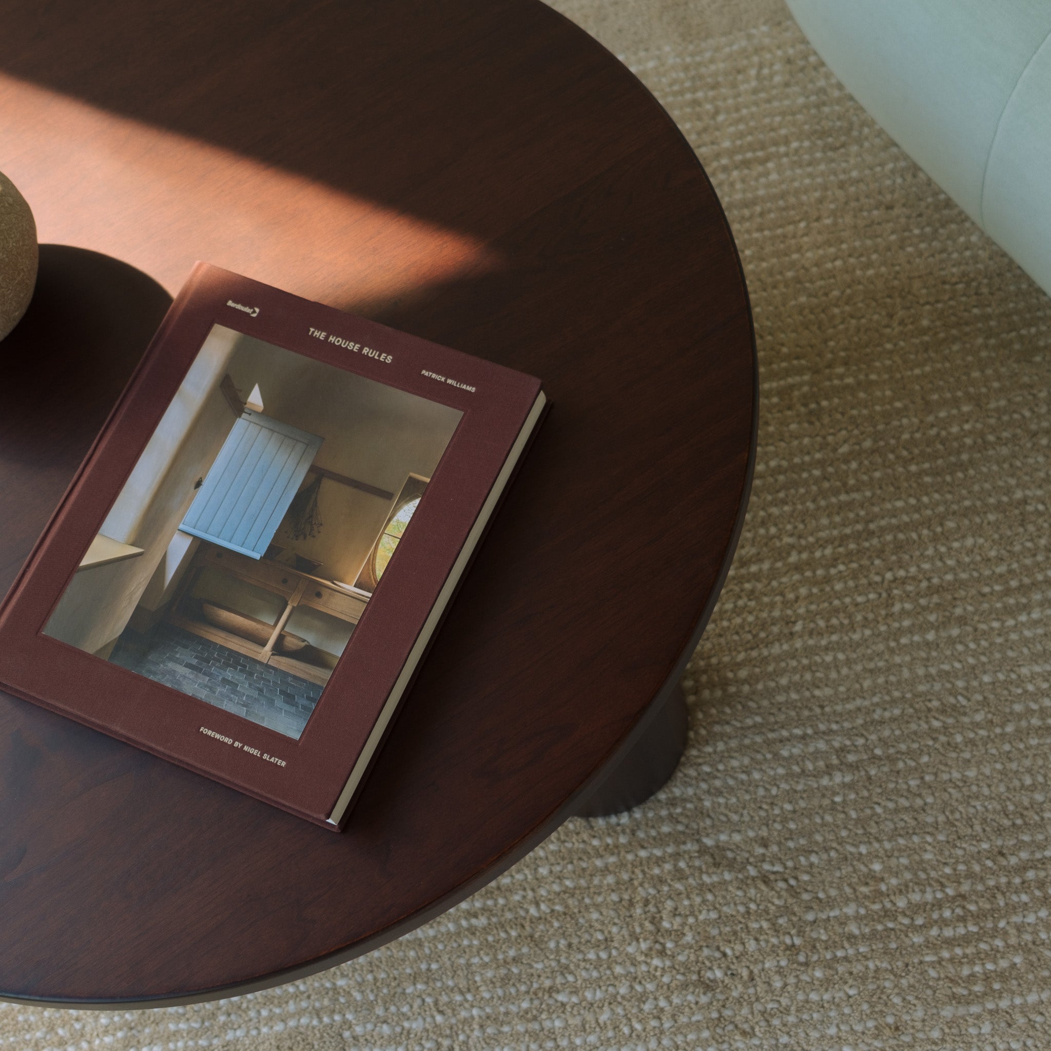 Gami round solid walnut coffee table with cylinder legs, sunlit tabletop and hardcover book on rug