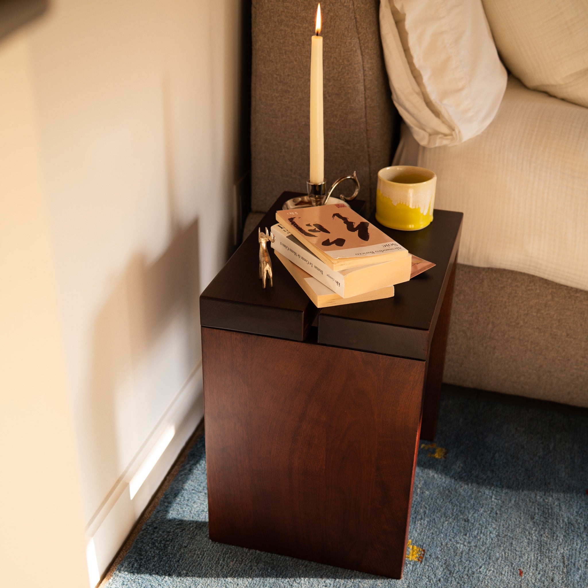 Mieux Lyster solid walnut stool used as a nightstand with candle and books beside a bed