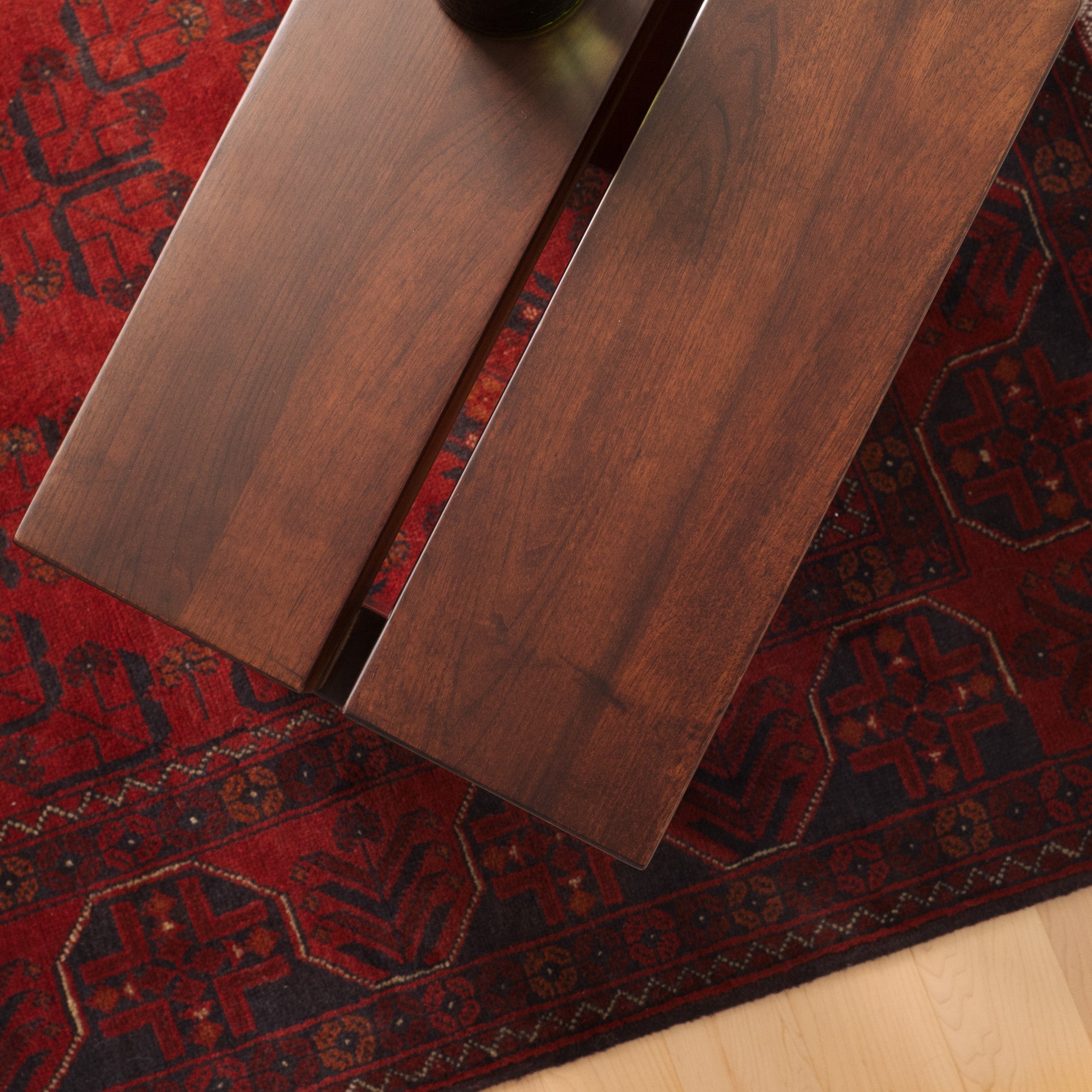 Mieux Lyster solid walnut stool on a red patterned rug