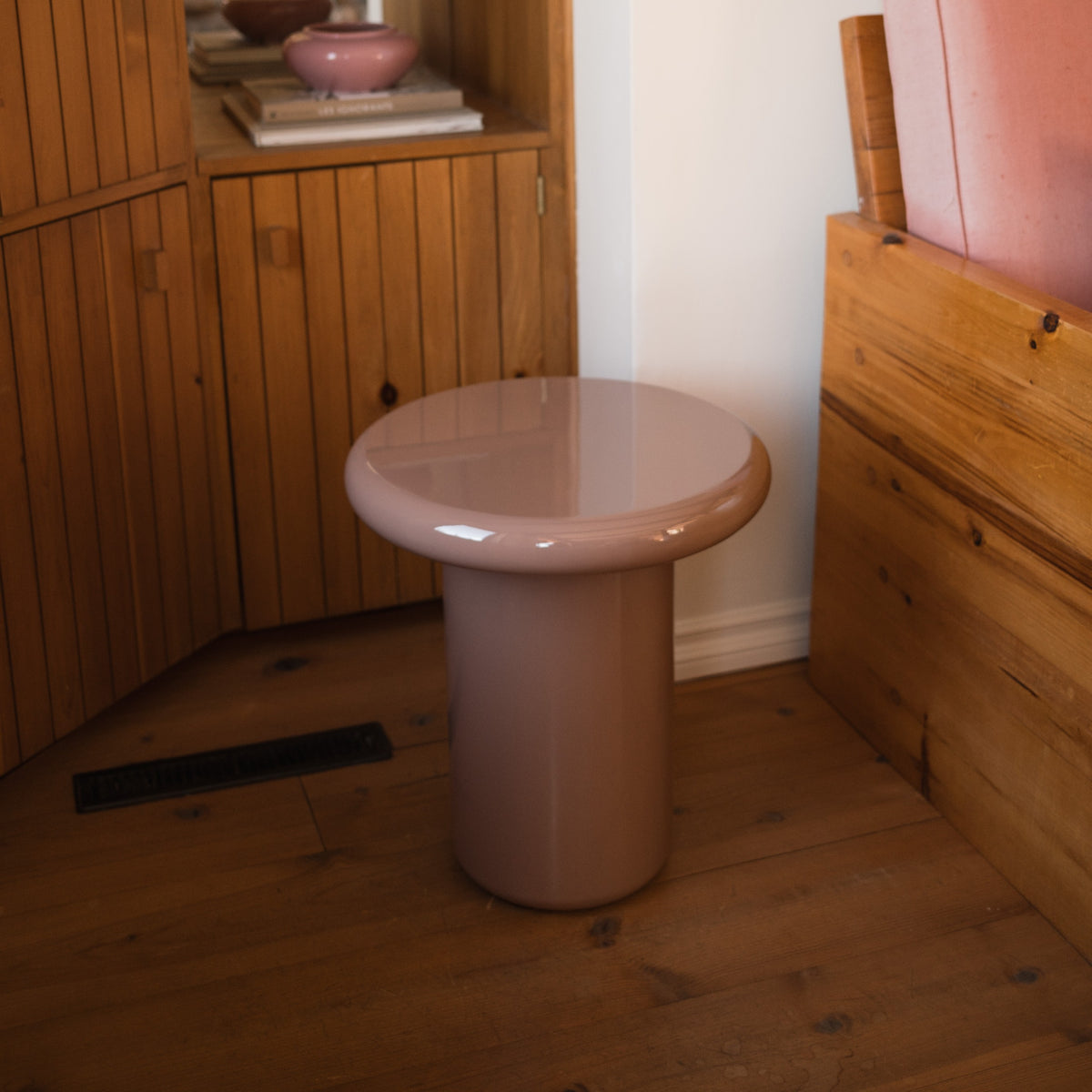 Mieux glossy, round side table in dusty pink, set in a rustic room with wooden floors and cabinetry.