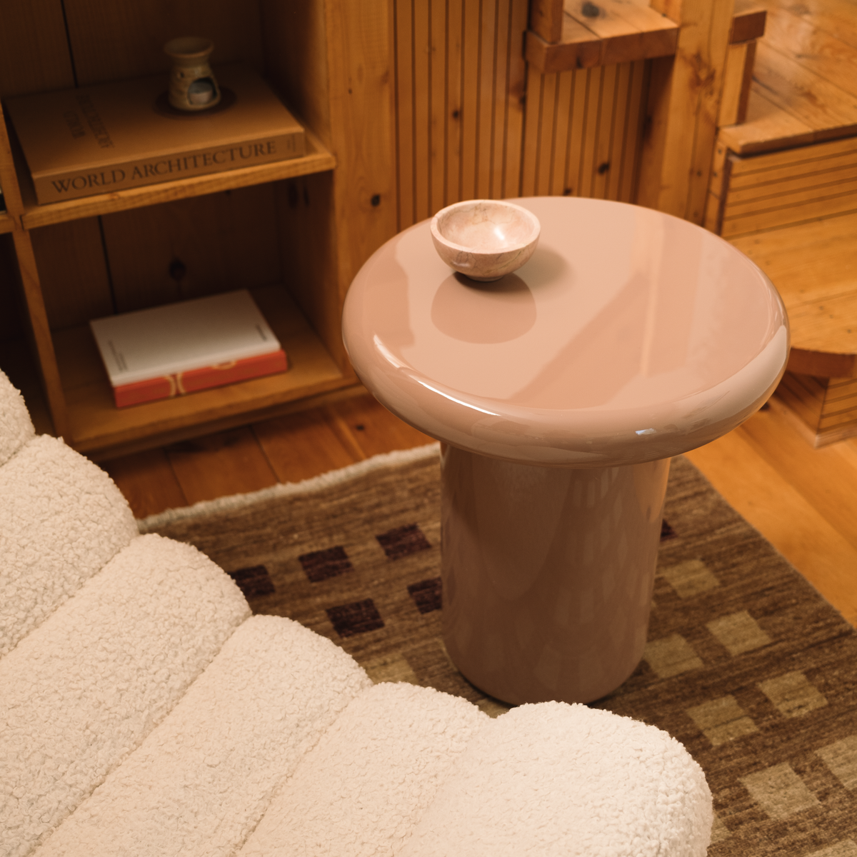 Mieux round mushroom-shaped high gloss side table in a dusty pink color, styled in a cozy wood-paneled room next to a white boucle chair.