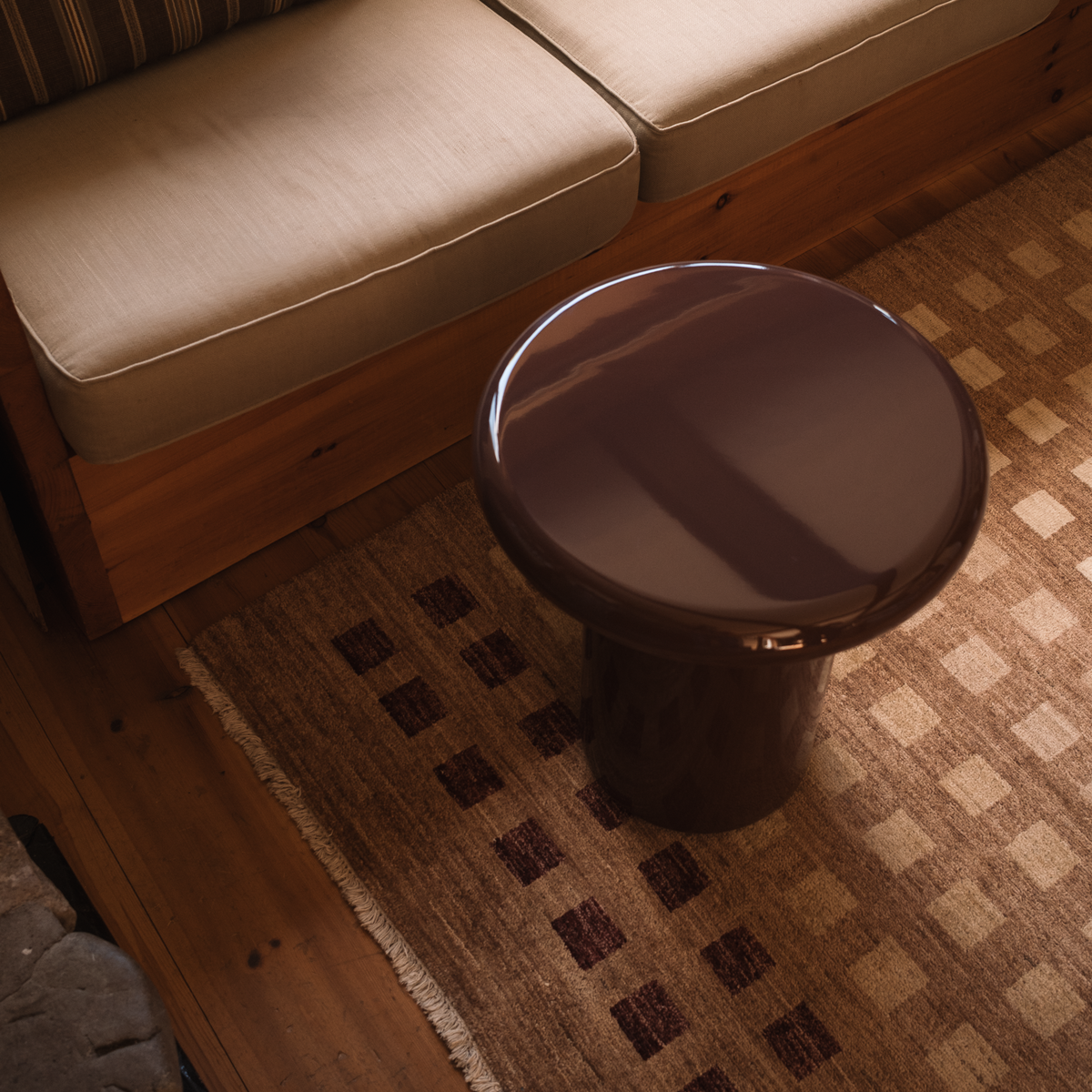 Mieux glossy dark red round side table in a living room setting, with a wooden bench and cushions visible in the background.