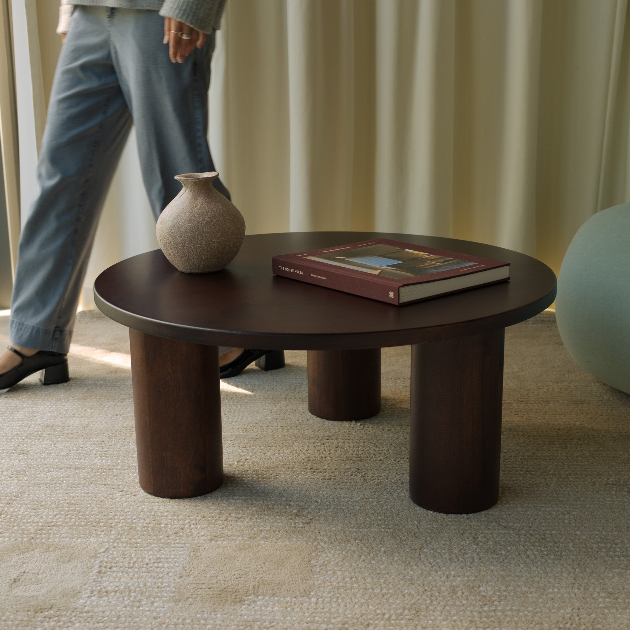 Gami round solid walnut coffee table with three cylinder chunky legs styled in a living room with vase and book