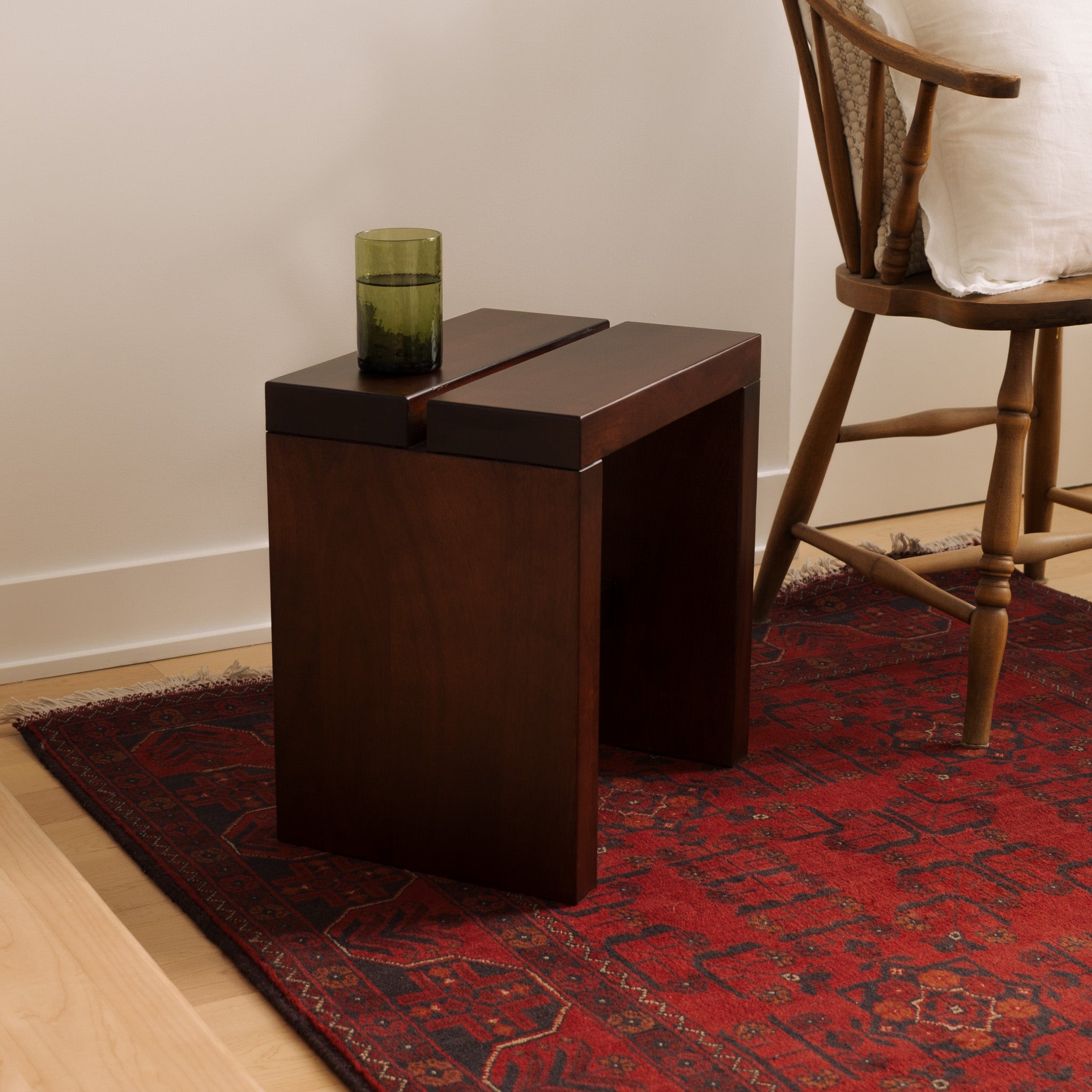 Mieux Lyster solid walnut stool with beside a wood chair on a red rug